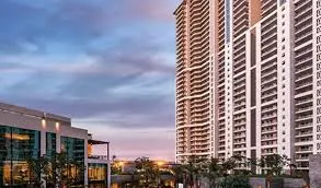Modern urban view of DLF The Arbour featuring high-rise residential towers with balconies and a commercial glass-front building surrounded by landscaped greenery.