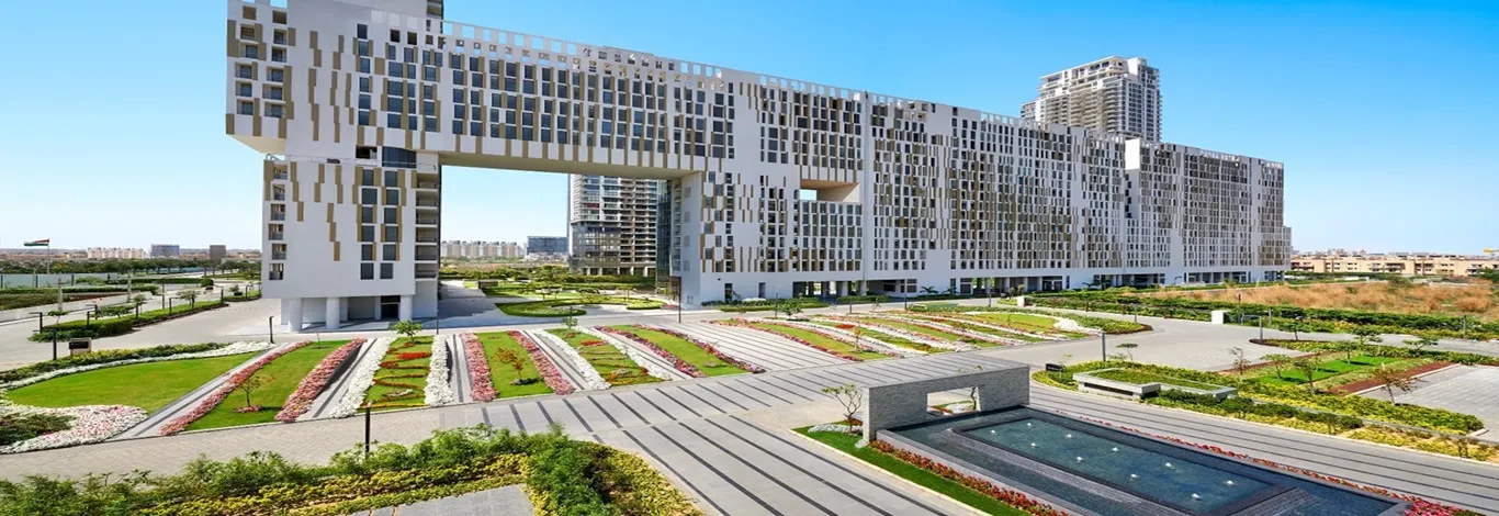 DLF The Dahlias modern architectural complex featuring striking twin towers connected by a horizontal section, with landscaped gardens, fountains, and a clear blue sky in the background.