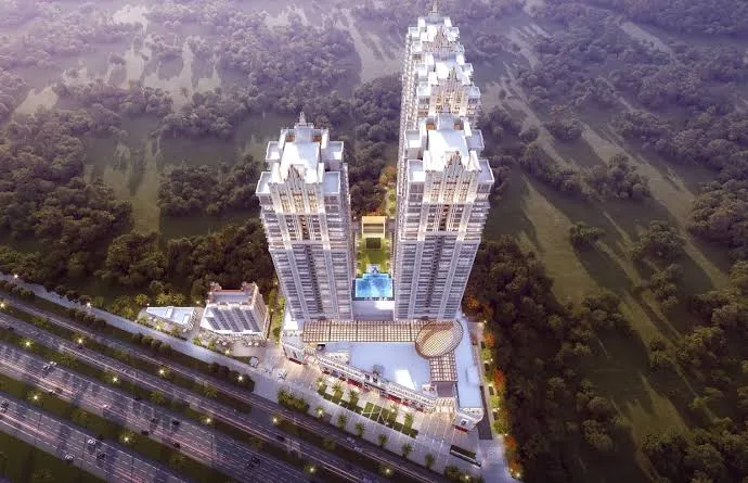 Aerial view of Hero Homes The Palatial with four illuminated towers, swimming pool, landscaped plaza, and surrounding forest.