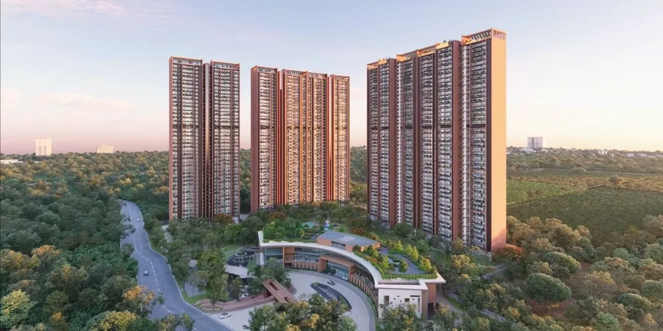 Sobha Aranya residential complex with tall high-rise towers surrounded by lush greenery, featuring a curved clubhouse entrance, landscaped gardens, and a circular driveway in a forested urban setting during daylight.